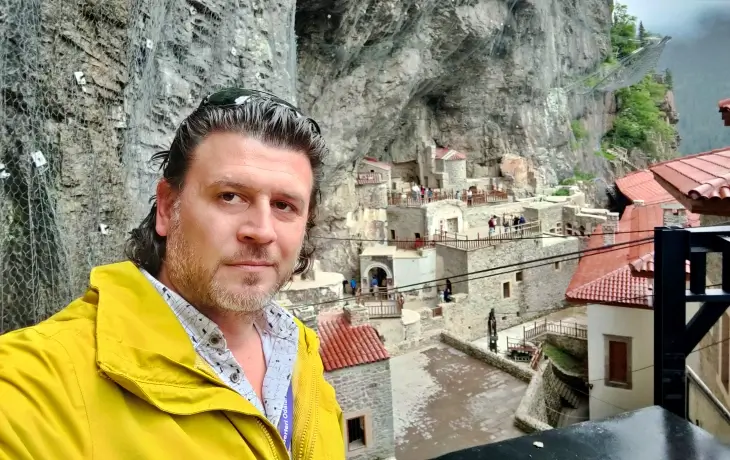 Sümela Manastırı avlusunda manastır kompleksini arka plana alarak poz veren bir ziyaretçi.